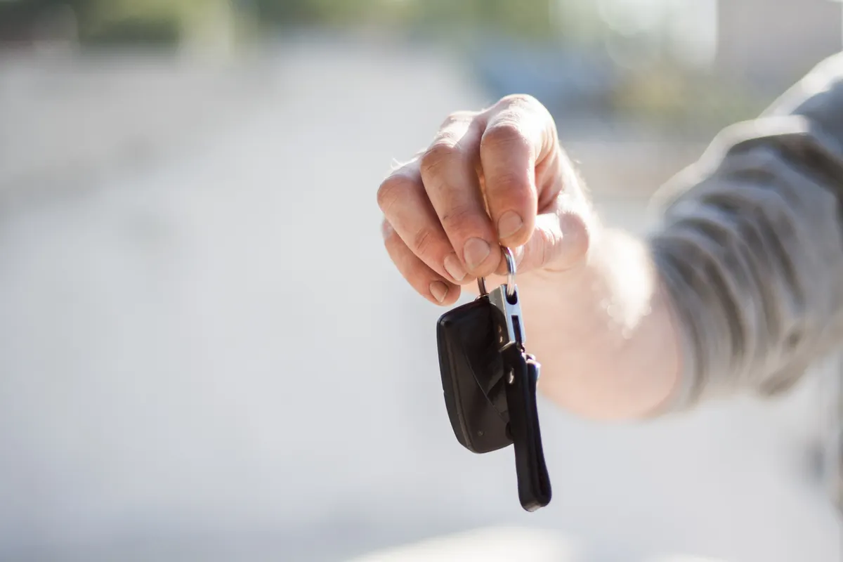 Schlüsselübergabe beim Fahrzeugübergabeprotokoll – Hand übergibt Autoschlüssel an eine andere Person